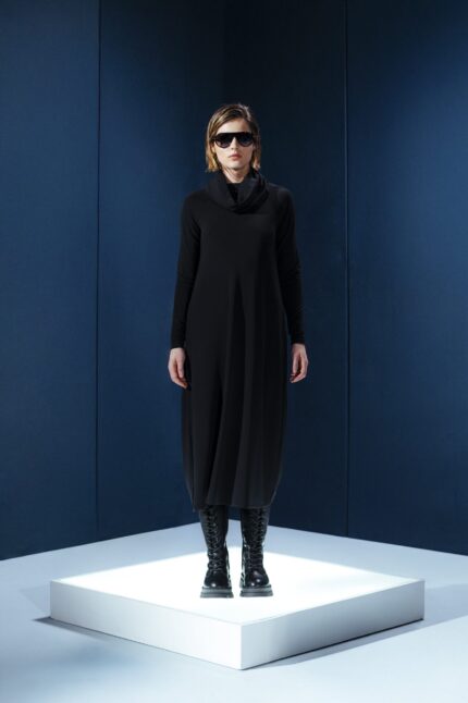 Vestido midi preto em jersey com mangas longas, gola drapeada e amarrações laterais. Silhueta ajustável com elegância e conforto.