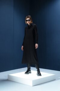 Vestido midi preto em jersey com mangas longas, gola drapeada e amarrações laterais. Silhueta ajustável com elegância e conforto.