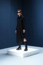 Vestido midi preto em jersey com mangas longas, gola drapeada e amarrações laterais. Silhueta ajustável com elegância e conforto.