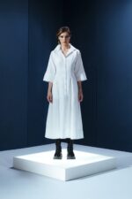 Vestido de tricoline branco com mangas 3/4 e detalhe de couro nas costas. Modelagem elegante com cintura marcada e recortes estruturados.