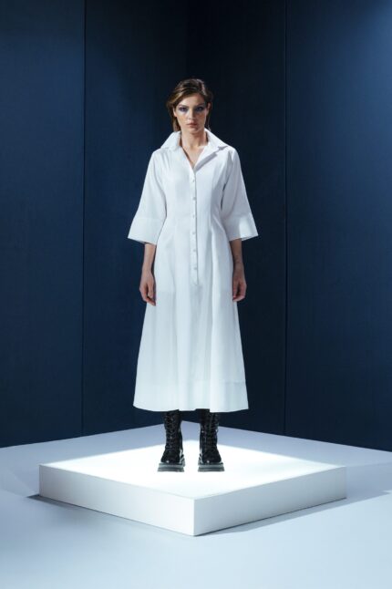 Vestido de tricoline branco com mangas 3/4 e detalhe de couro nas costas. Modelagem elegante com cintura marcada e recortes estruturados.