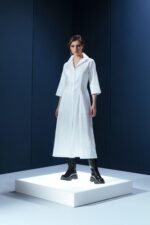 Vestido de tricoline branco com mangas 3/4 e detalhe de couro nas costas. Modelagem elegante com cintura marcada e recortes estruturados.