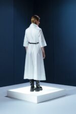 Vestido de tricoline branco com mangas 3/4 e detalhe de couro nas costas. Modelagem elegante com cintura marcada e recortes estruturados.