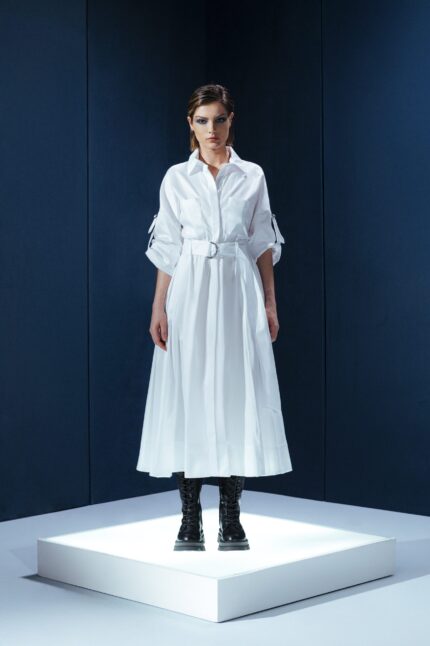 Vestido de tricoline branco com mangas ajustáveis, bolsos frontais e cinto. Modelagem ampla, sofisticada e versátil para diversas ocasiões.