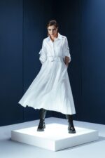 Vestido de tricoline branco com mangas ajustáveis, bolsos frontais e cinto. Modelagem ampla, sofisticada e versátil para diversas ocasiões.