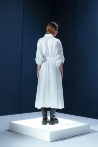 Vestido de tricoline branco com mangas ajustáveis, bolsos frontais e cinto. Modelagem ampla, sofisticada e versátil para diversas ocasiões.