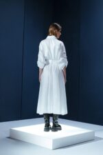 Vestido de tricoline branco com mangas ajustáveis, bolsos frontais e cinto. Modelagem ampla, sofisticada e versátil para diversas ocasiões.