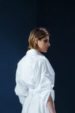 Vestido de tricoline branco com mangas ajustáveis, bolsos frontais e cinto. Modelagem ampla, sofisticada e versátil para diversas ocasiões.