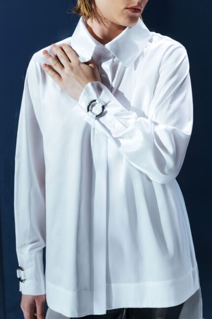 Camisa em tricoline branca com argola de metal no punho. Silhueta clássica com detalhe contemporâneo e toque de alfaiataria minimalista.