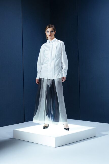 Camisa de tricoline com gola turca e pregas frontais. Silhueta limpa com detalhes arquitetônicos que revelam sofisticação contemporânea.