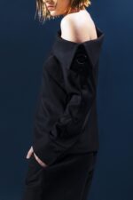 Camisa preta de lã fria com decote assimétrico, argola metálica e botões funcionais ao longo da manga. Estrutura elegante com proposta versátil.