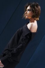 Camisa preta de lã fria com decote assimétrico, argola metálica e botões funcionais ao longo da manga. Estrutura elegante com proposta versátil.